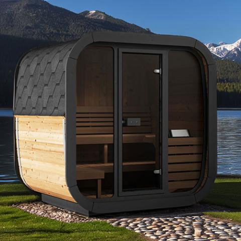 Portable sauna with wooden interior and black exterior by a body of water with mountains in the background